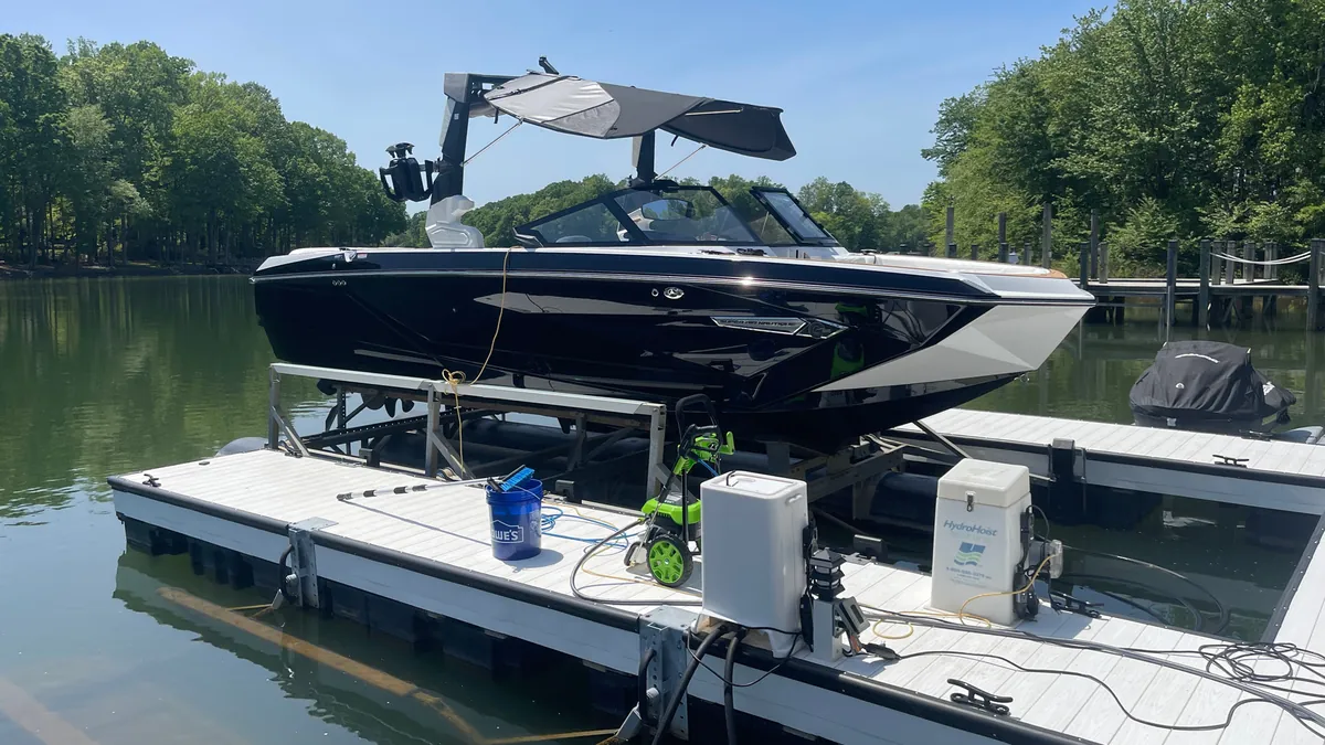 Black wake boat on a floating lift at a Lake Norman dock, with our pressure washer and gear set up beside it